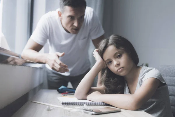 De dark-haired meisje zit aan de tafel en onverschillig, terwijl haar vader schreeuwen naar haar kijkt — Stockfoto