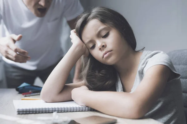 Schimpft der Vater auf seine Tochter, die traurig mit dem Kopf in der Hand am Tisch sitzt — Stockfoto