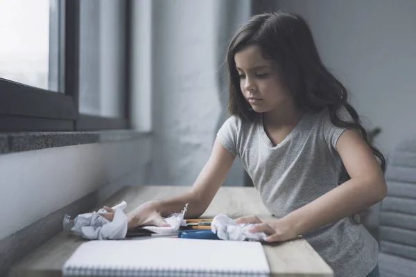 Een meisje in de dark-haired harken in een stapel van dingen die liggen op een kleine tafel, dat in de buurt van het venster staat — Stockfoto