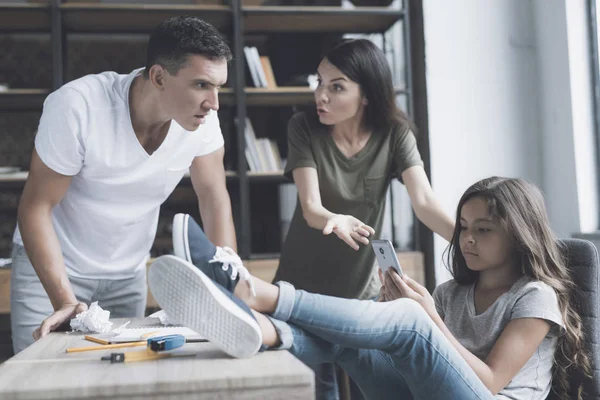 Padre y madre regañan a su hija, que los ignora y mira en el teléfono inteligente, poniendo sus pies sobre la mesa — Foto de Stock