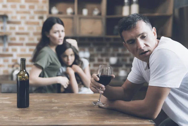 Um homem com vergonha se afasta de sua esposa e filha, que olham reprovadamente para ele enquanto ele bebe — Fotografia de Stock