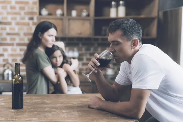 The woman hugs the girl and looks reproachfully at the man who sits next to him and drinks wine