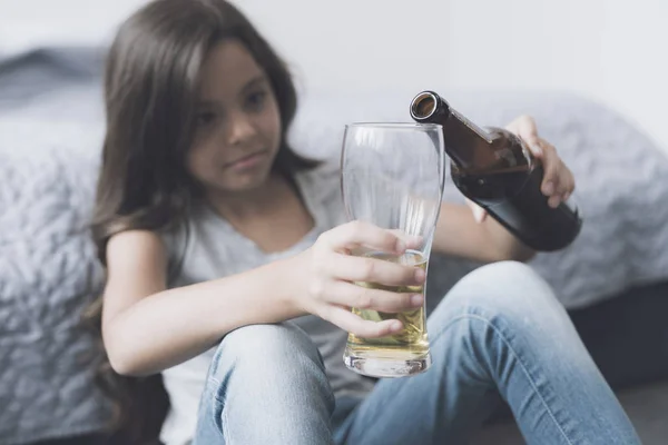 La fille aux cheveux bruns s'assoit près du lit et se verse une bière dans un verre — Photo