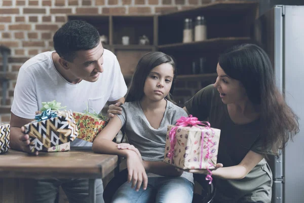 Una chica triste se sienta en una silla, y un hombre y una mujer alegres la mastican con regalos para ella — Foto de Stock