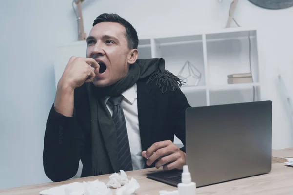 Un hombre enfermo está sentado en su lugar de trabajo en la oficina. Se rocía en la garganta de un spray médico — Foto de Stock
