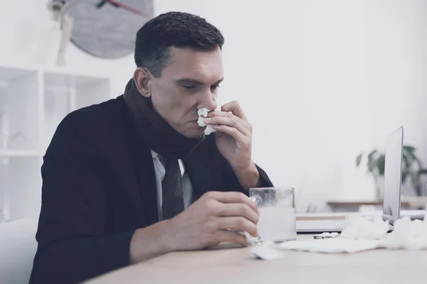 Хвора людина сидить на своєму робочому місці в офісі. Він дме ніс у серветку — стокове фото