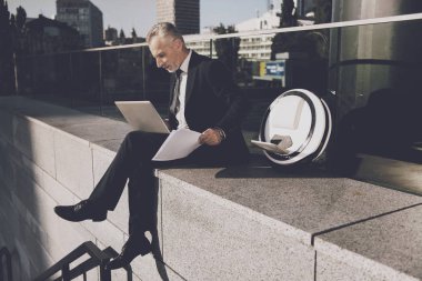 Bir adam bir parapetin üzerinde oturan bir dizüstü bilgisayar üzerinde çalışıyor. Onun mono-wheel