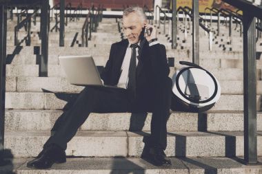Sıkı iş takım elbiseli saygın bir yaşlı adam office merdivenlerinde oturur. O onun mono-tekerlek yanındaki bir tablet üzerinde çalışıyor