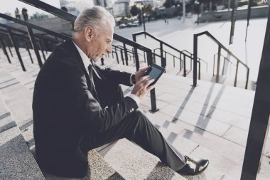 Sıkı iş takım elbiseli saygın bir yaşlı adam office merdivenlerinde oturur. O onun mono-tekerlek yanındaki bir tablet üzerinde çalışıyor
