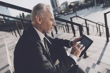 Sıkı iş takım elbiseli saygın bir yaşlı adam office merdivenlerinde oturur. O onun mono-tekerlek yanındaki bir tablet üzerinde çalışıyor