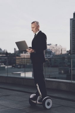 İhtiyar bir gyroboard biniyor ve açık bir dizüstü elinde tutuyor. O sıkı iş kıyafeti var