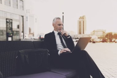 Yaşlı adam sokakta kanepede oturuyor. Kucağında bir dizüstü bilgisayar tutuyor