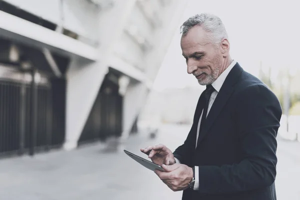 Empresário em um terno preto está procurando em um tablet . — Fotografia de Stock