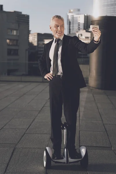 El anciano en un estricto traje de negocios hace selfie mientras monta un giroscopio —  Fotos de Stock