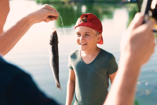 Um homem mostra ao menino em um boné vermelho um peixe que ele acabou de pegar em sua fiação — Fotografia de Stock