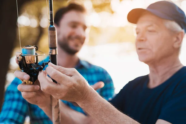 Close up. The old man inspects the fishing spinning spool. A man looks at the old man — Stock Photo, Image