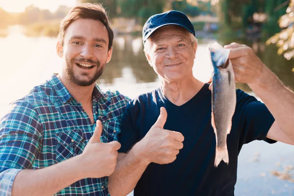 Polegares para cima. Um homem está ao lado de um velho que está segurando um peixe que ele acabou de pegar — Fotografia de Stock