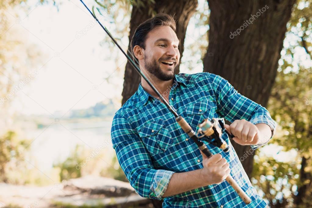 A happy man in a blue shirt tries to pull the fish out of the river with the help of spinning