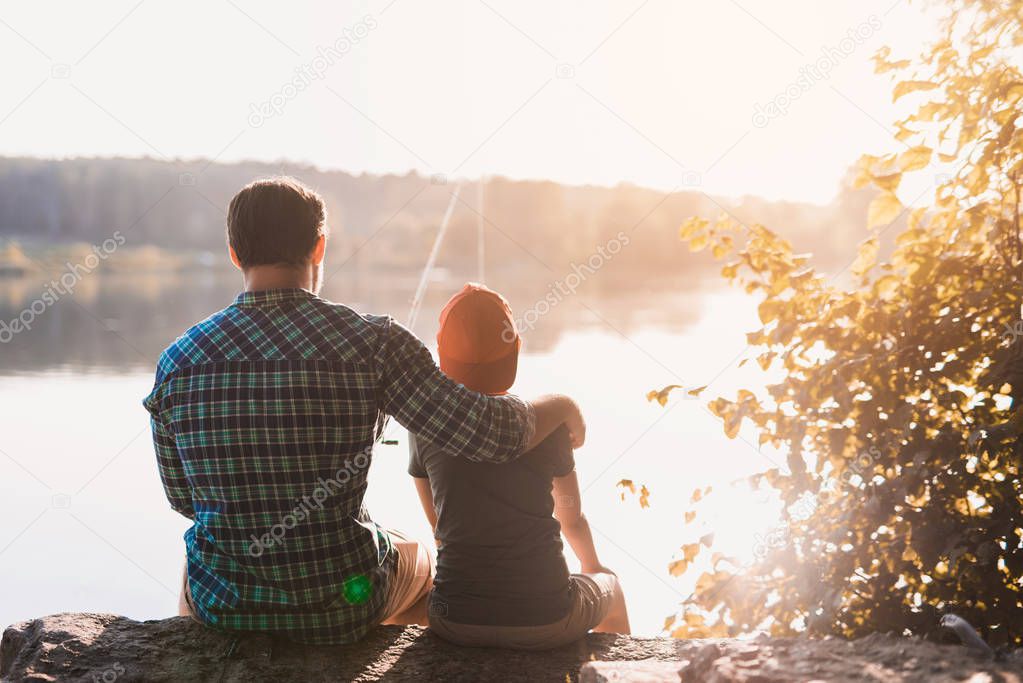 Father and son are fishing, sitting on the riverbank against the backdrop of dawn