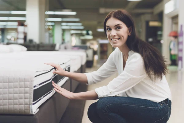 Una donna sceglie un materasso in un negozio. Lei si siede accanto a lui e lo esamina — Foto Stock