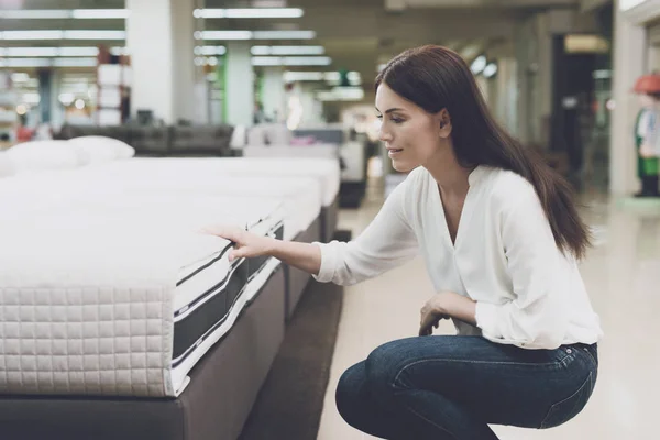 A woman chooses a mattress in a store. She sits next to him and examines him — Stock Photo, Image
