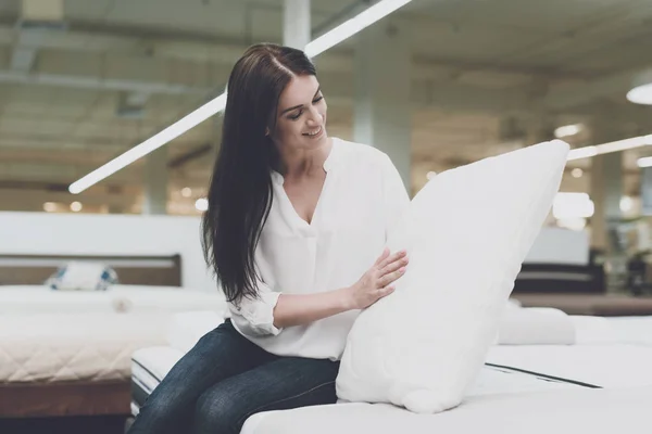 A woman picks herself a pillow in a large store. She sits on the bed and examines her. She sits and examines her — Stock Photo, Image