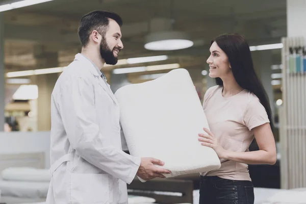 Ортопедический консультант помогает женщине выбрать ортопедическую подушку. Он показывает ей один из вариантов подушек — стоковое фото