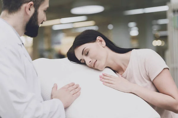 El consultor ortopédico ayuda a una mujer a elegir una almohada ortopédica. Él le muestra una de las opciones de almohada —  Fotos de Stock