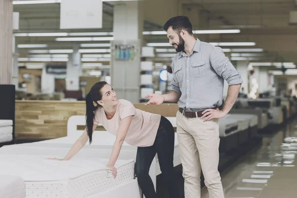 Una pareja elige un colchón en la tienda. Una mujer señala a uno de ellos. Un hombre está a la espera —  Fotos de Stock