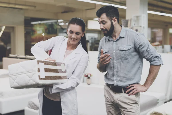 En ortopedisk kvinna visar mannen ett prov av madrassen han vill köpa — Stockfoto