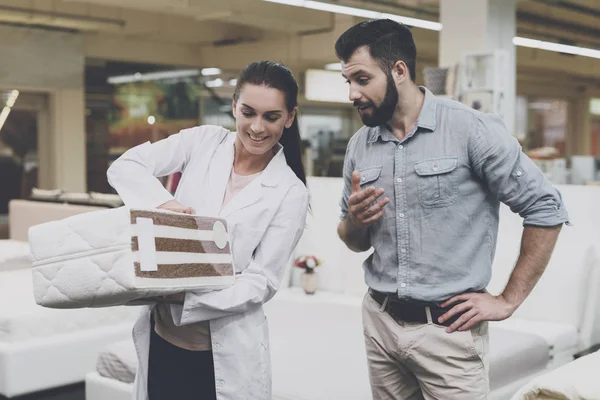 Una mujer ortopédica le muestra al hombre una muestra del colchón que quiere comprar —  Fotos de Stock