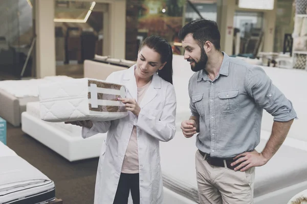 An orthopedic woman shows the man a sample of the mattress he wants to buy — Stock Photo, Image