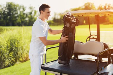 Bir adam beyaz giysili duruyor ve bir çanta golf kulüpleri golf sahası bagajdan için ortaya çıkarır