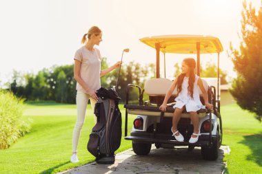 Kız bir golf arabası gövde yanında otururken bir kadın onun çantasından bir golf kulübü çeker
