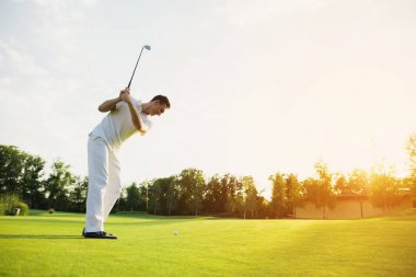 Beyaz elbiseli bir adam golf oynuyor. O sopayı alıp vurmaya hazırlanıyor