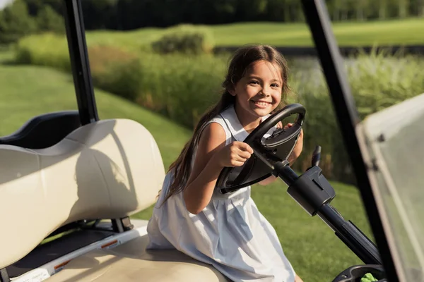 Niña con un vestido brillante sonriendo mientras está sentada al volante de un coche de golf —  Fotos de Stock