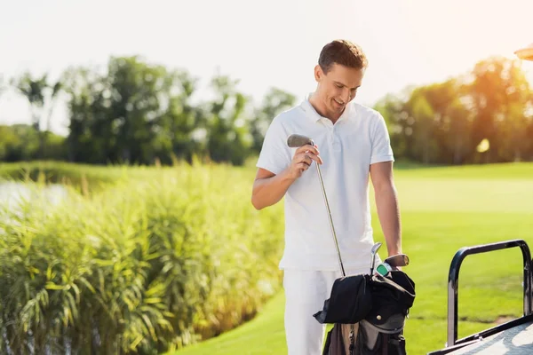 一个穿着白衣服的男人站在一辆高尔夫球车后面, 从包里挑出一根棍子来玩。 — 图库照片