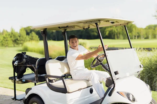 Lycklig man på en vit golfbil tittar in i kameran och visar en hand framåt — Stockfoto