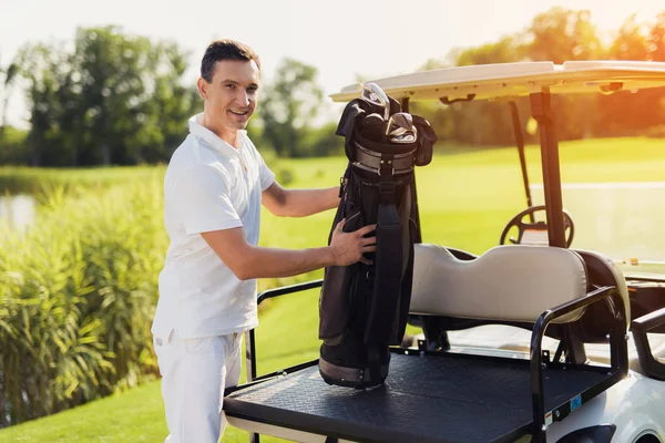 Un hombre con un traje blanco sostiene una bolsa con palos de golf, que se encuentra en el maletero del campo de golf —  Fotos de Stock
