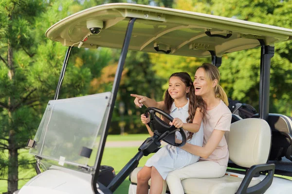 The girl is sitting on her lap near a woman who runs a golf cart. The girl points the direction to where to go — Stock Photo, Image