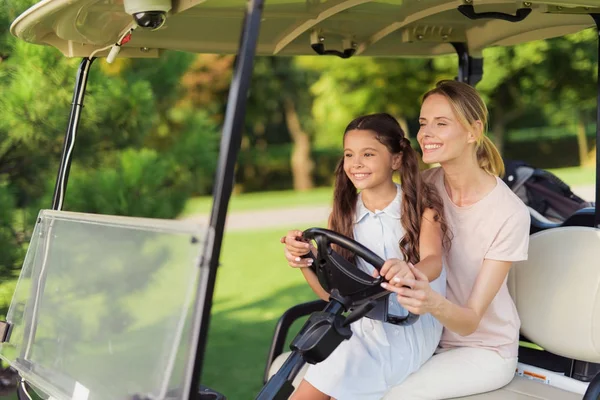 The girl is sitting on the lap of a woman. Together they control a golf cart — Stock Photo, Image