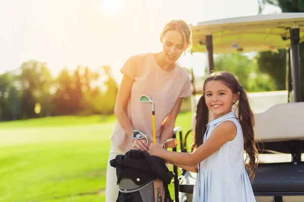 En kvinna och en flicka få golfklubbar ur påsen. Flickan tittar på kameran — Stockfoto