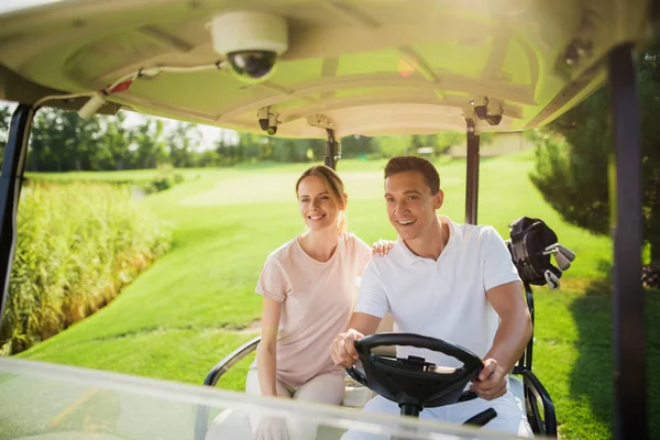 Pareja feliz monta en un carro de golf blanco jugando golf. La mujer puso su mano sobre el hombro del hombre —  Fotos de Stock