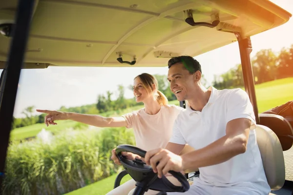 Casal montando um carrinho de golfe branco no campo de golfe — Fotografia de Stock