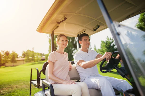 Una pareja va a jugar golf. Un hombre se sienta al volante de un coche de golf blanco, una mujer se sienta cerca —  Fotos de Stock