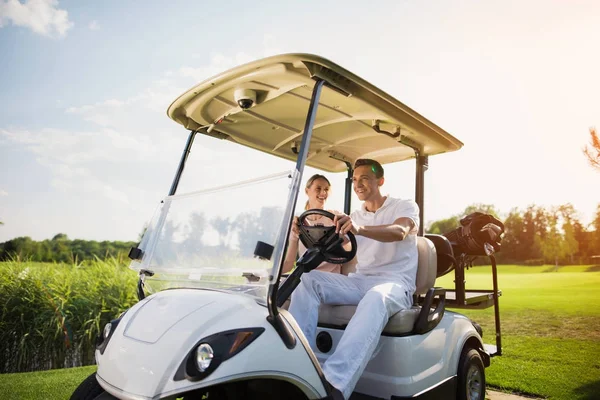 快乐的男人和女人坐在一个白色的高尔夫球车, 这是站在高尔夫俱乐部的道路 — 图库照片