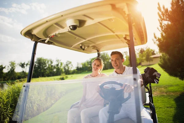 En man sitter på förarsätet av golfbil, en kvinna sitter bredvid passagerarsätet — Stockfoto