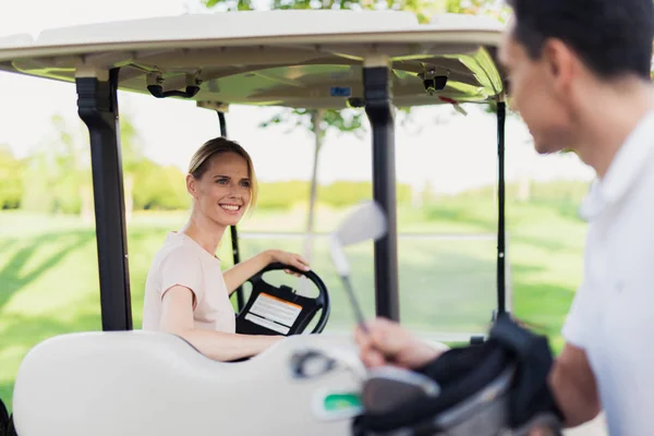 Un hombre saca un palo de golf de la bolsa, una mujer se sienta al volante de un coche de golf —  Fotos de Stock