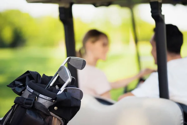 Ferme la photo. Clubs de golf au premier plan, homme avec une femme dans une voiturette de golf sur un fond — Photo