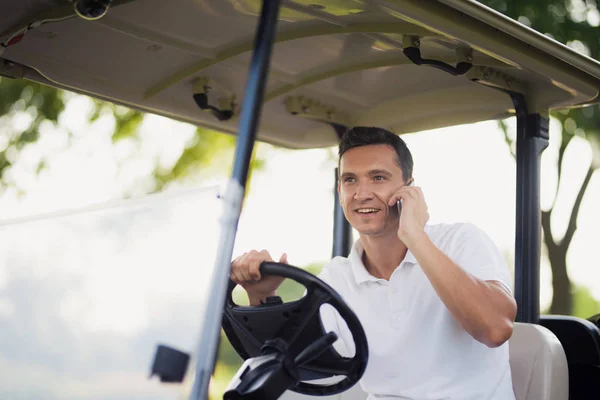 Un hombre está conduciendo un coche de golf y hablando con alguien en un teléfono inteligente —  Fotos de Stock